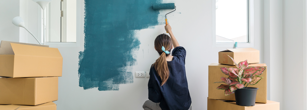 Vrouw schildert een muur blauw van een kamer met dozen op de achtergrond